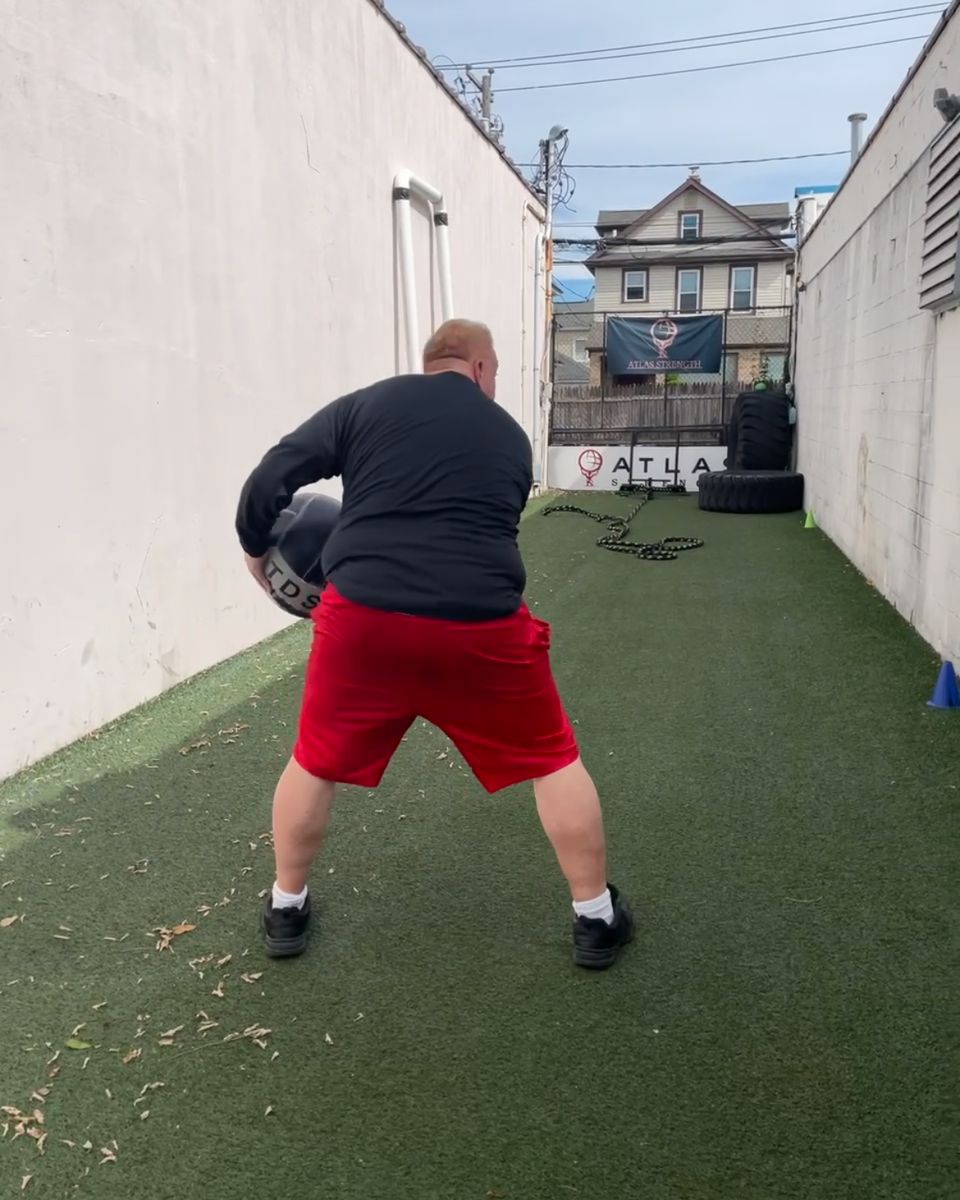 Client throwing a medicine ball on the outdoor turf at Atlas Strength
