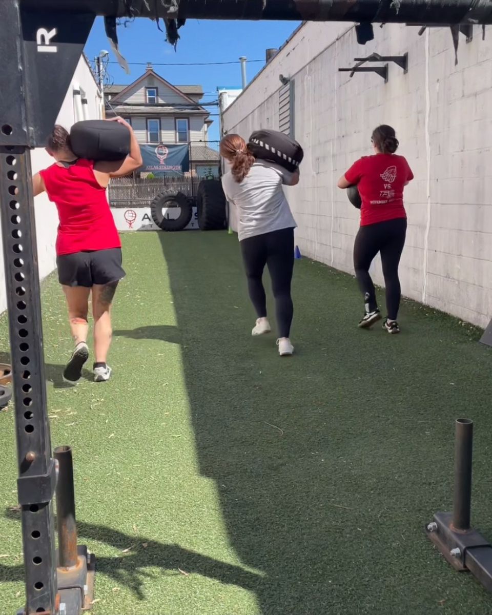 Three clients carrying sandbags on the outdoor turf during a semi-private session