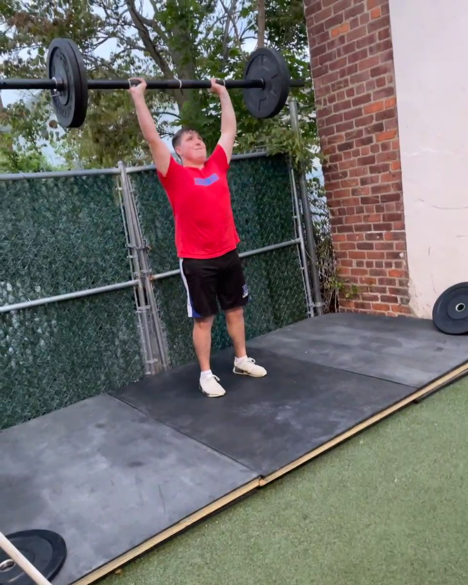 Smiling teen holding a barbell overhead at Atlas Strength