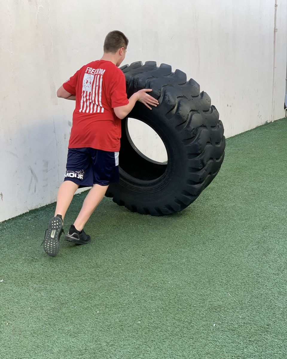 Teen rolling a big tire on the turf