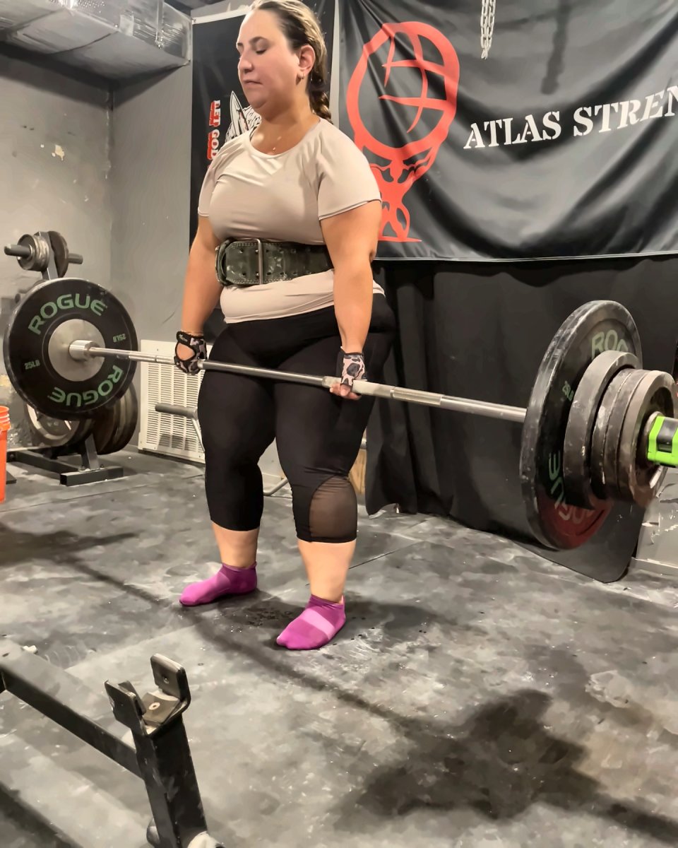 Client locking out a deadlift in front of the Atlas Strength banner