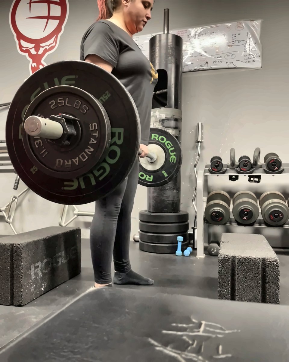 Woman locking out a deadlift in front of the Atlas Strength logo