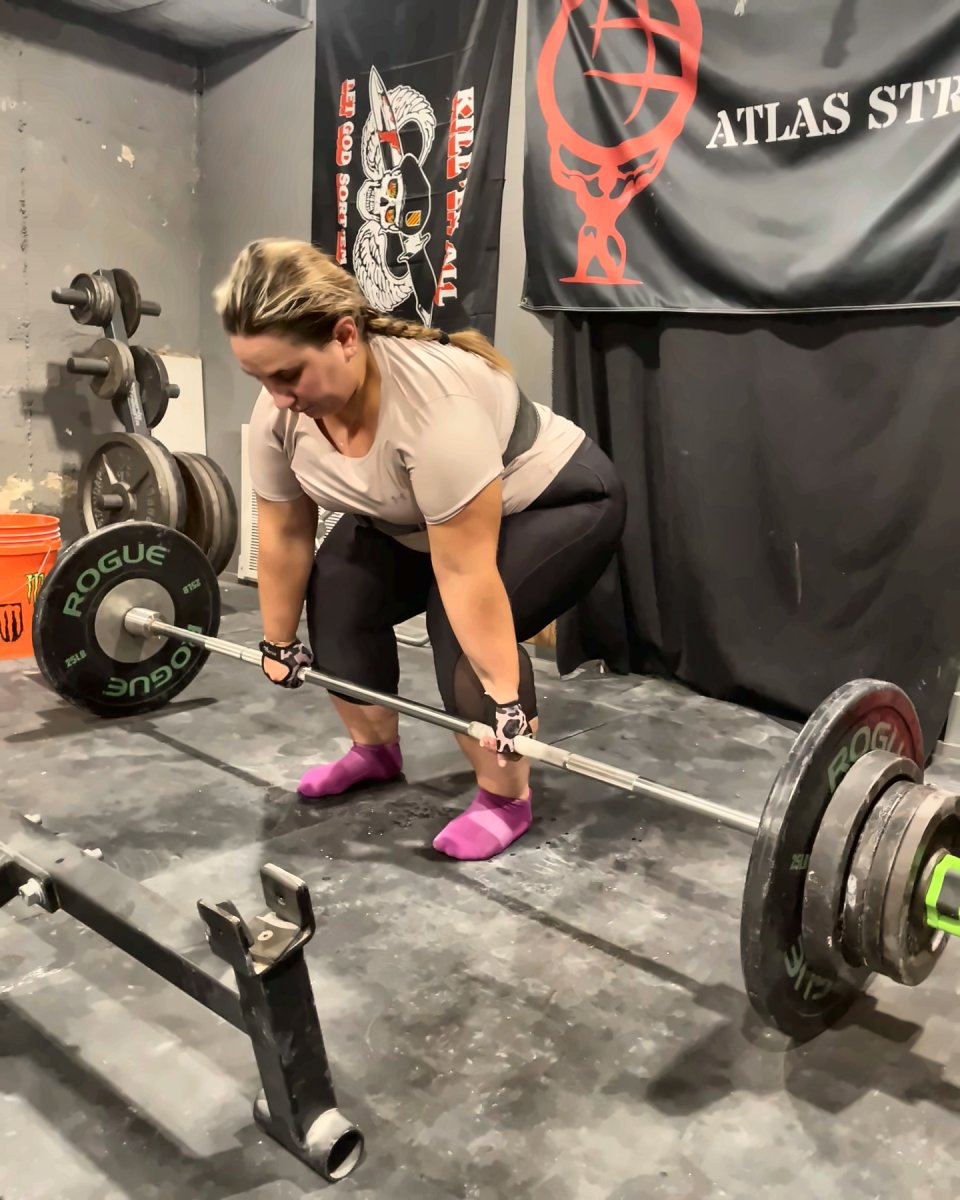 Client setting up for a deadlift in front of the Atlas Strength banner