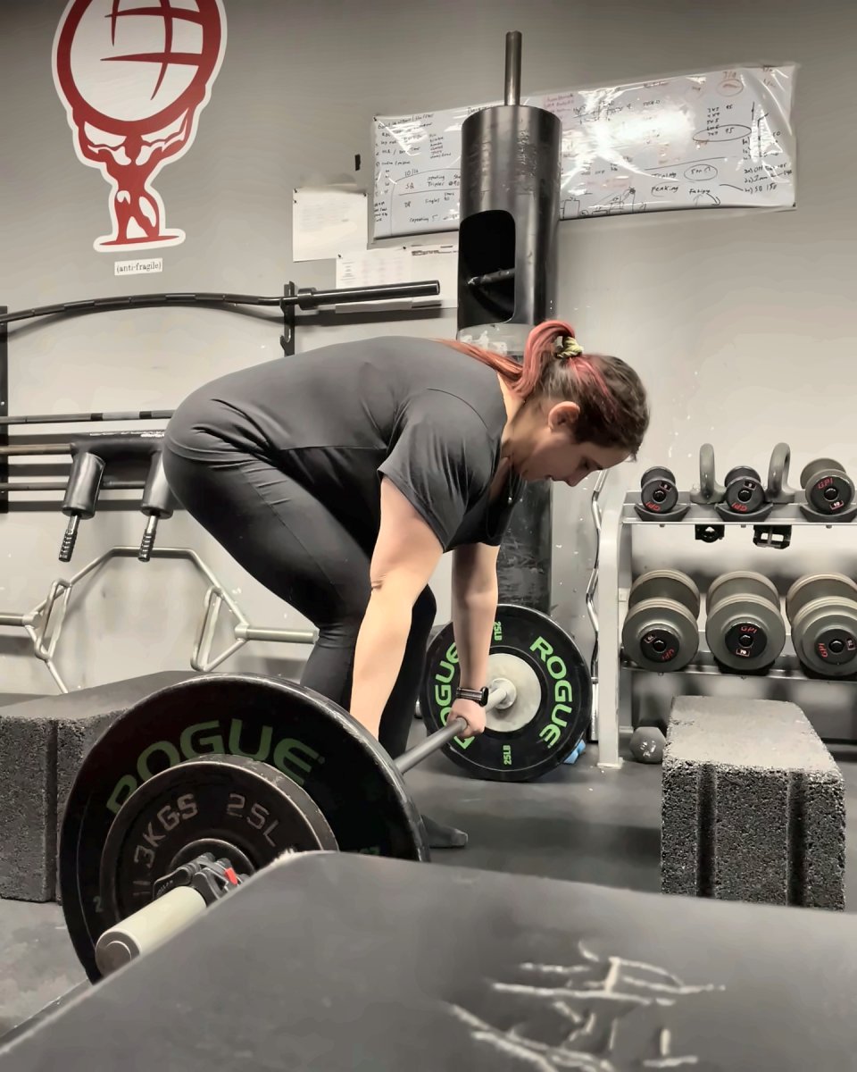 Woman setting up for a deadlift in front of the Atlas Strength logo
