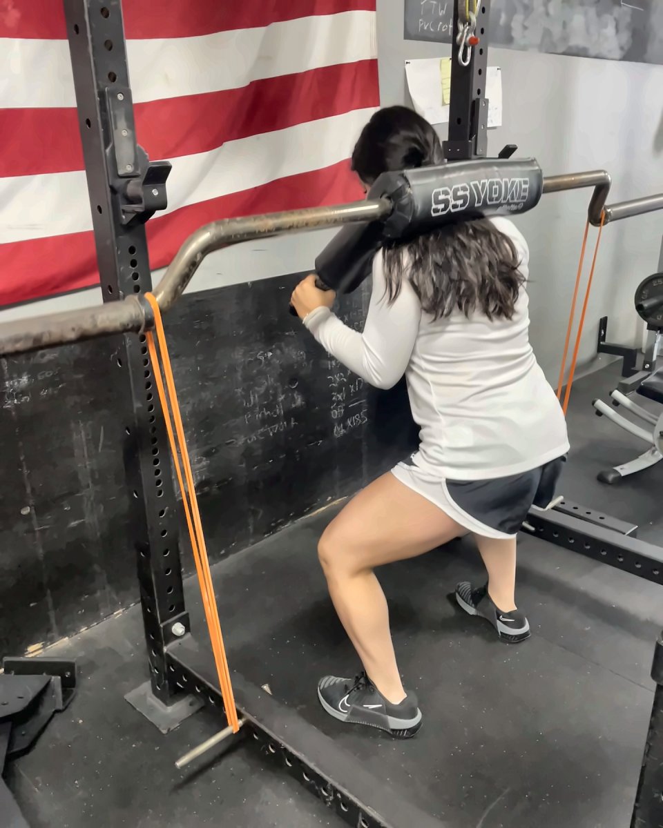 Woman squatting with a safety squat bar in the rack