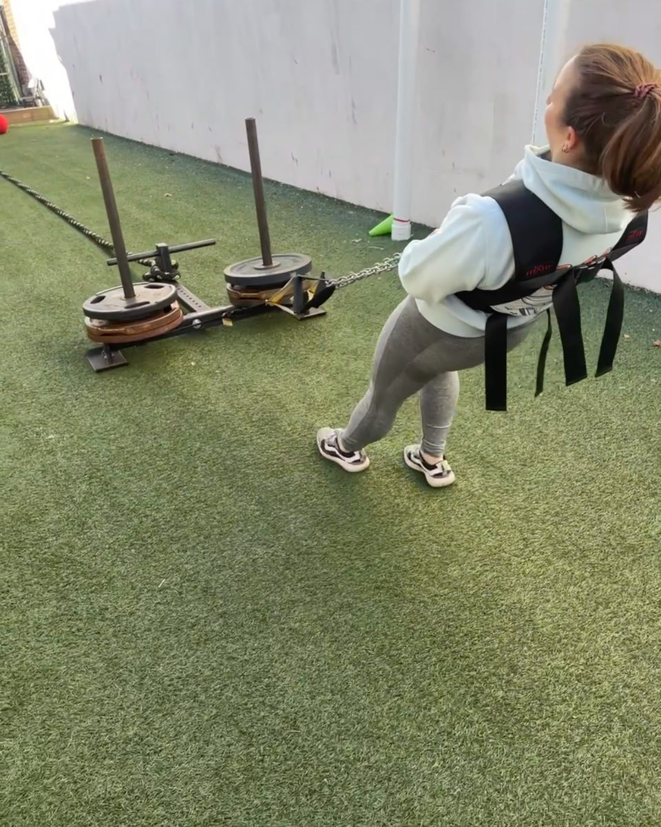 Woman dragging a loaded sled in a harness on the turf