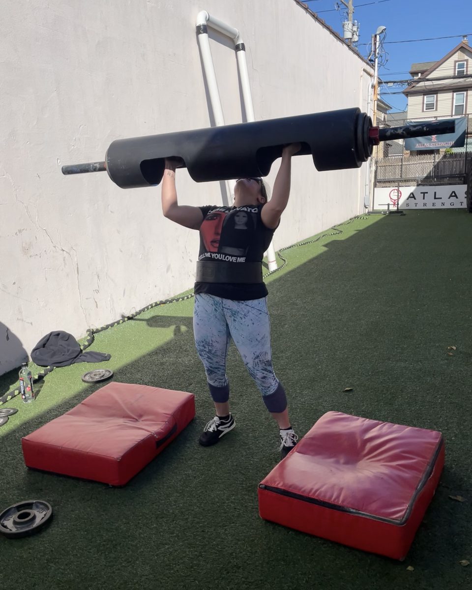 Woman locking out a strongman log press on the Atlas Strength turf