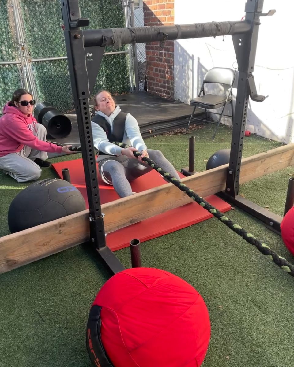 Woman doing a seated rope pull while a teammate helps